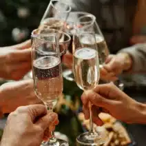 A group of people clink champagne glasses in a toast, with food and a decorated tree visible in the background.