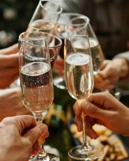 A group of people clink champagne glasses in a toast, with food and a decorated tree visible in the background.