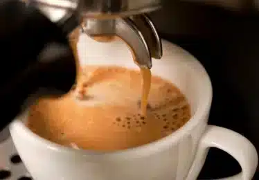 Close-up of fresh espresso pouring from a machine into a white ceramic cup, with a layer of crema forming on top.