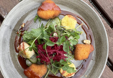 Goat’s cheese salad served with mixed greens, pickled red onion, and a balsamic glaze, enjoyed on the outdoor terrace at The Walter Raleigh Hotel.