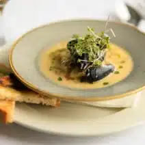 Seafood showder in a bowl showing mussels and watercress garnish. on a plate with toast