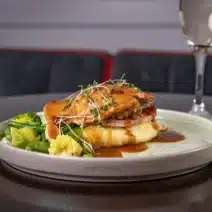 Roast meat with gravy and vegetables and mashed potatoes on a plate with a glass of Prosecco