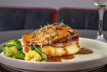 Roast meat with gravy and vegetables and mashed potatoes on a plate with a glass of Prosecco