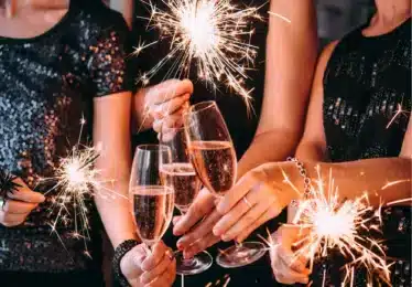 Three people holding sparklers and toasting with champagne glasses, dressed in festive attire.