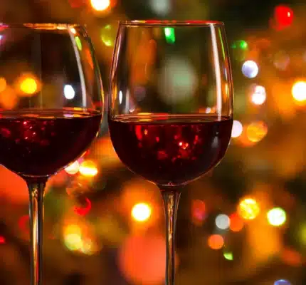 Two glasses of red wine against a background of colorful, out-of-focus lights.