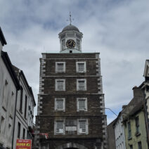 The historic Clock Gate Tower in Youghal, County Cork, standing tall above the narrow street with surrounding colorful and traditional buildings.