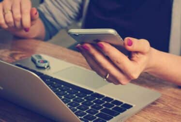 person holding phone while infront of a laptop