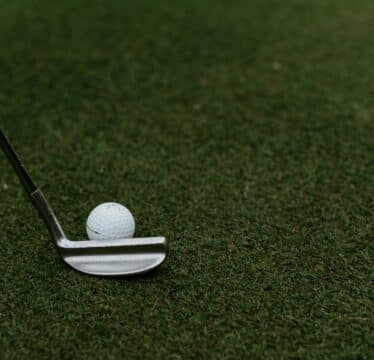 Golf club and golf ball on green pitch