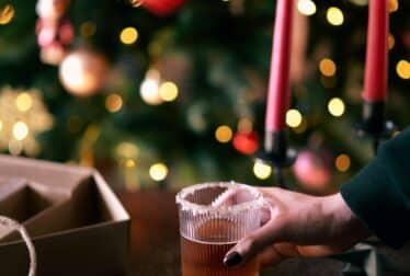 womans hand with a drink infront of a christmas tree and two candles