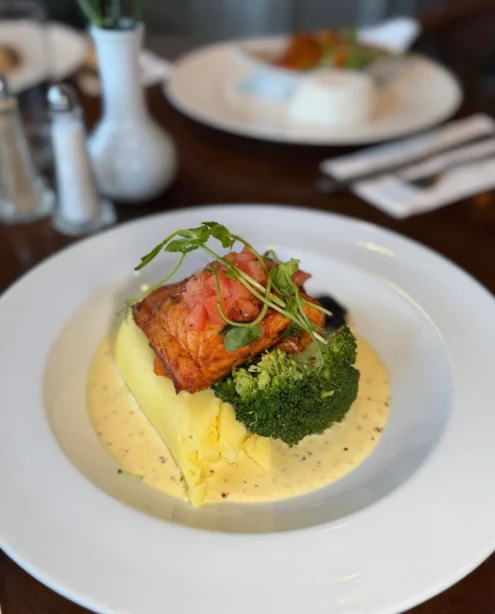 Pan-seared salmon with crushed potatoes, steamed broccoli and creamy mustard sauce, garnished with diced tomatoes and microgreens in a hotel restaurant dining setting